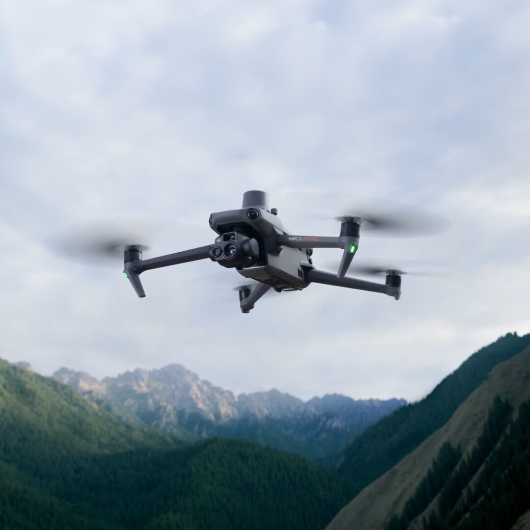 A black and silver drone flying over some mountains