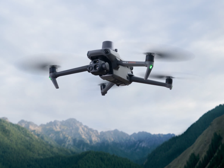 A black and silver drone flying over some mountains.